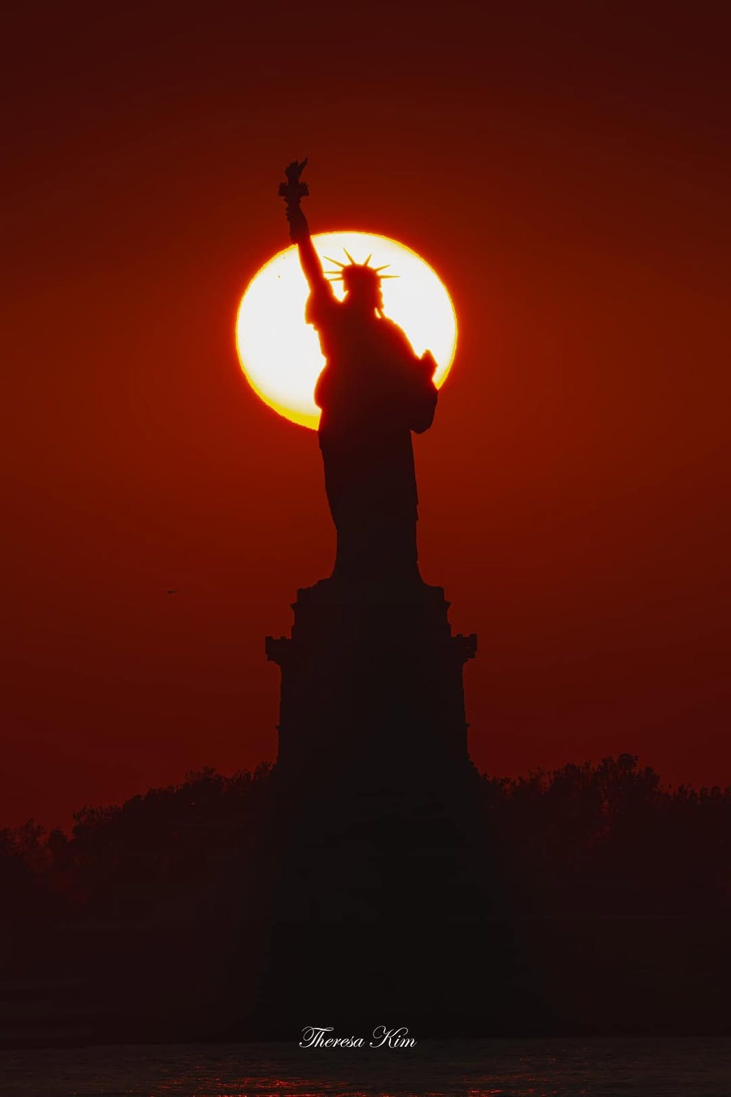 Statue of Liberty silhouetted inside the glowing disk of the setting sun