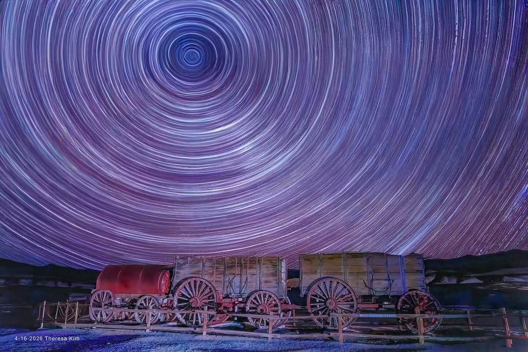 Star trails circling above old wooden wagons at night