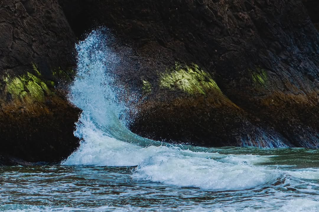 Wave curling and crashing against dark coastal rocks