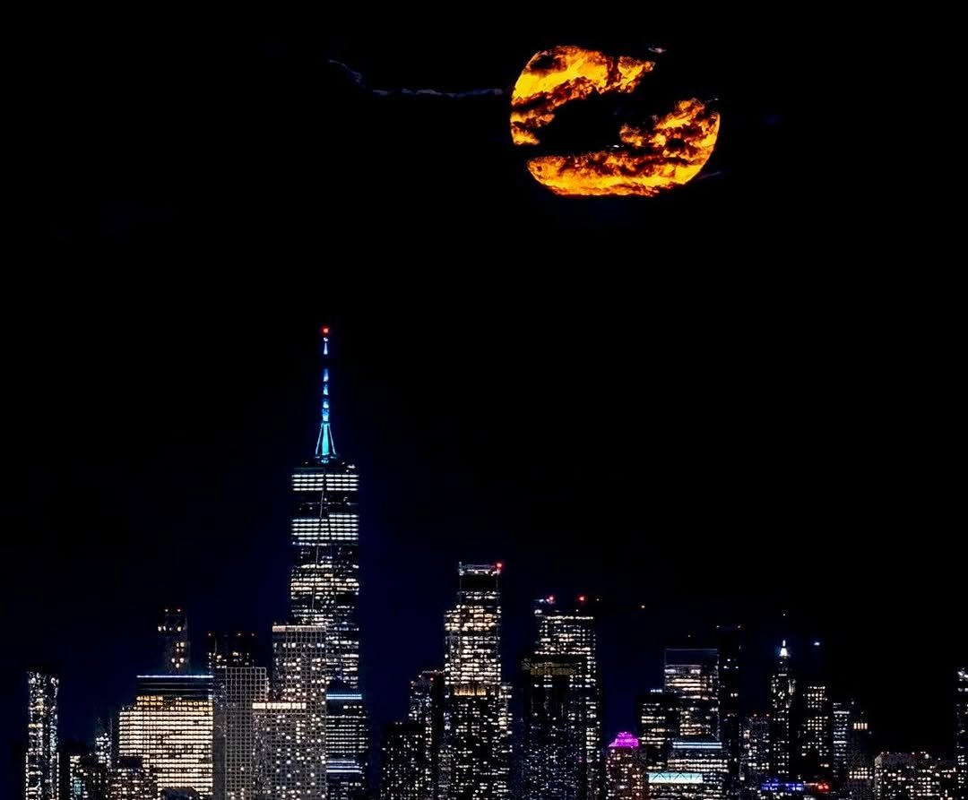 Eclipsed orange moon above the lit skyline of Lower Manhattan